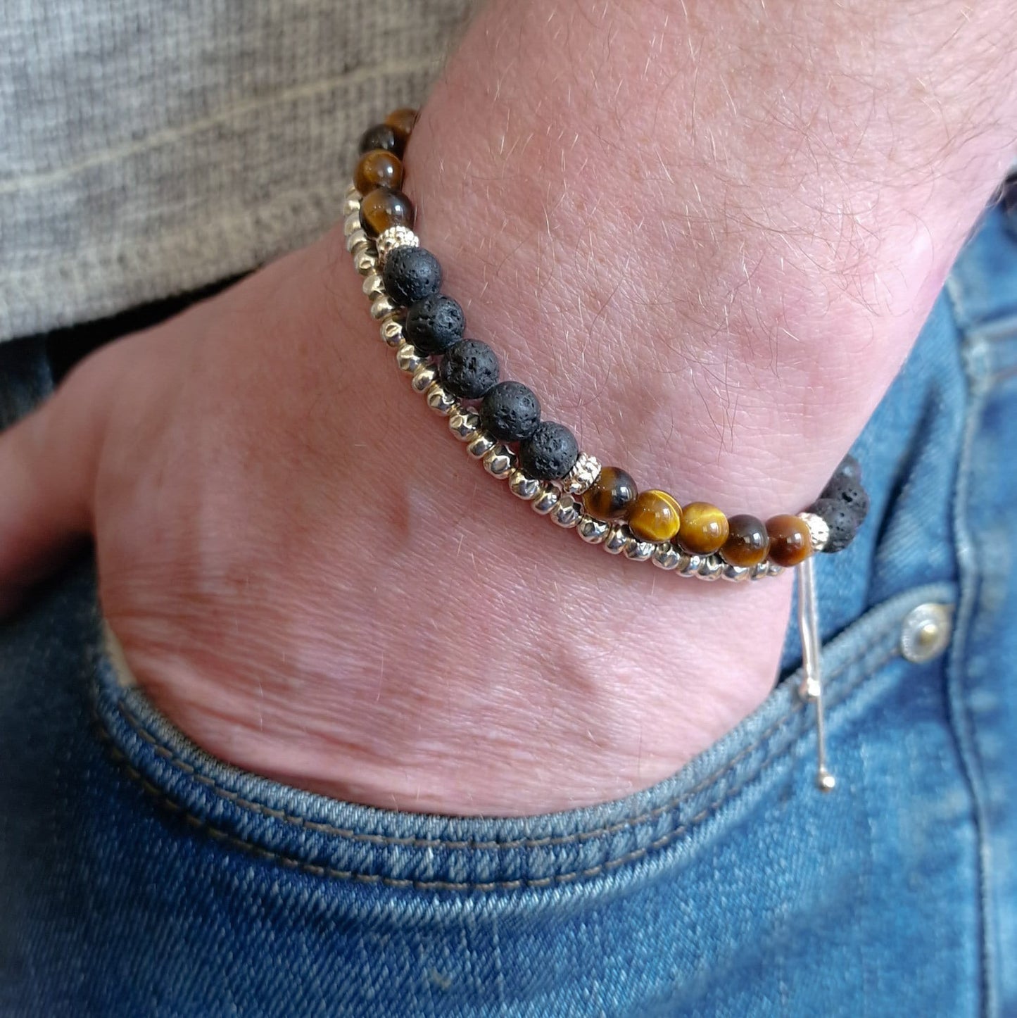 Tigers eye and silver bracelet on man's wrist. Man's hand is in the pocket of jeans.