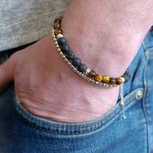 Tigers eye and silver bracelet on man's wrist.  Man's hand is in the pocket of jeans.