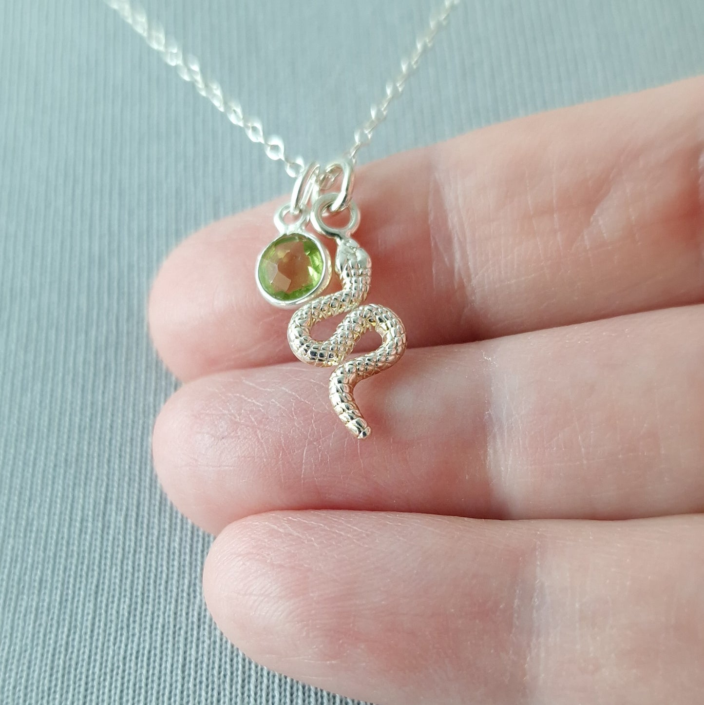 Close up of a silver snake pendant and peridot birthstone necklace