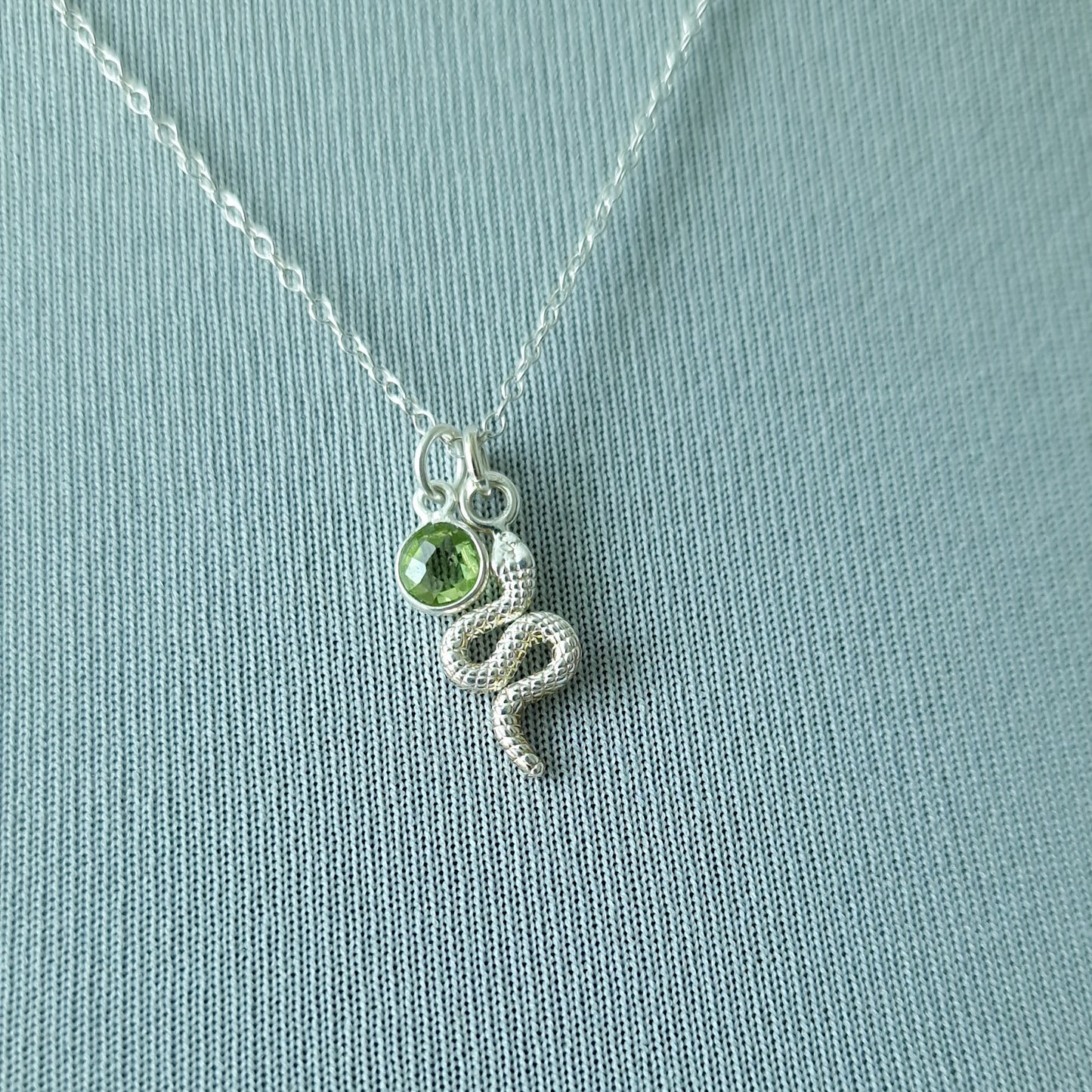 Close up of a silver snake pendant and peridot birthstone necklace