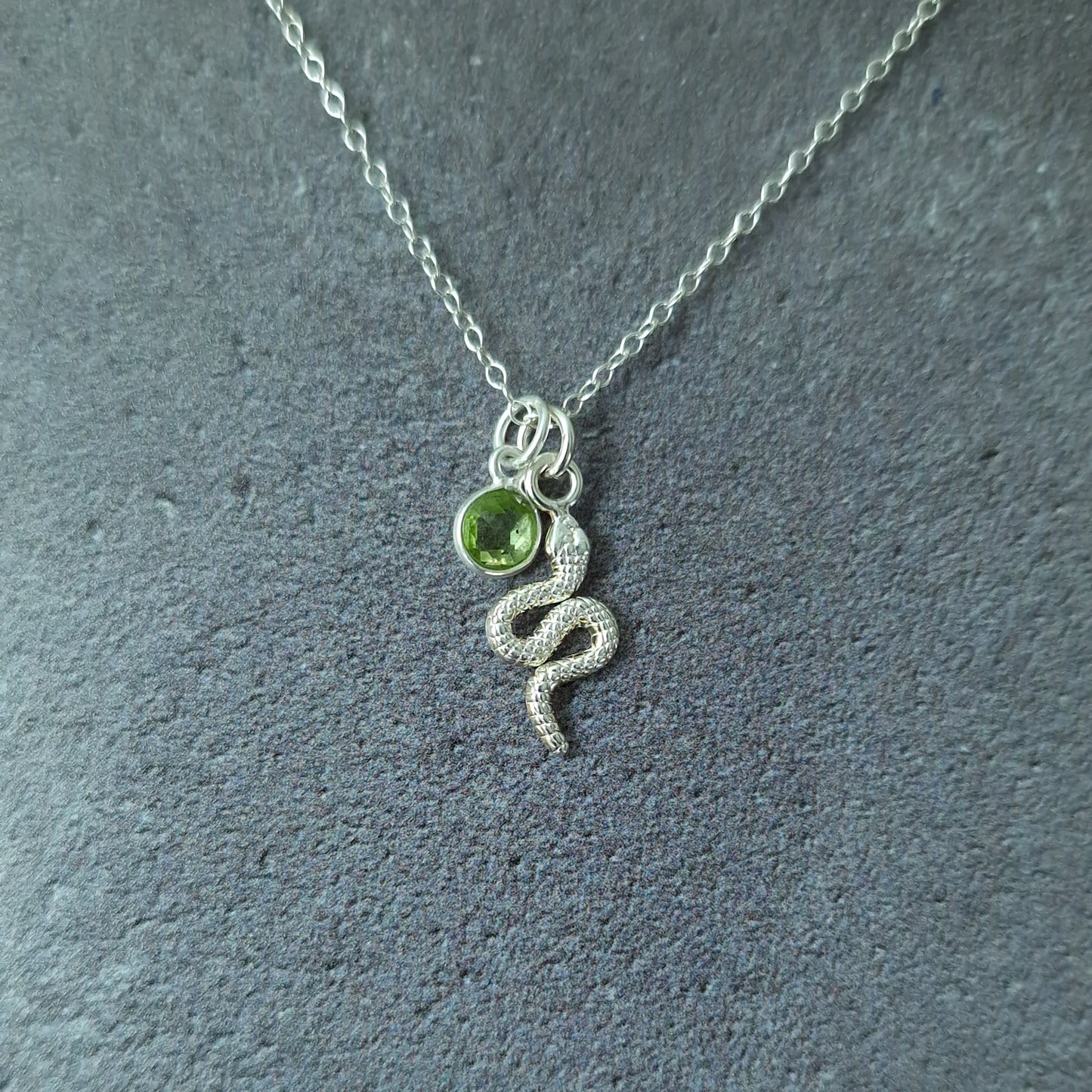 Close up of a silver snake pendant and peridot birthstone necklace