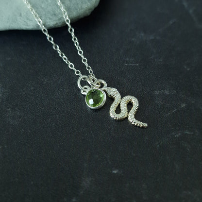 Close up of a silver snake pendant and peridot birthstone necklace