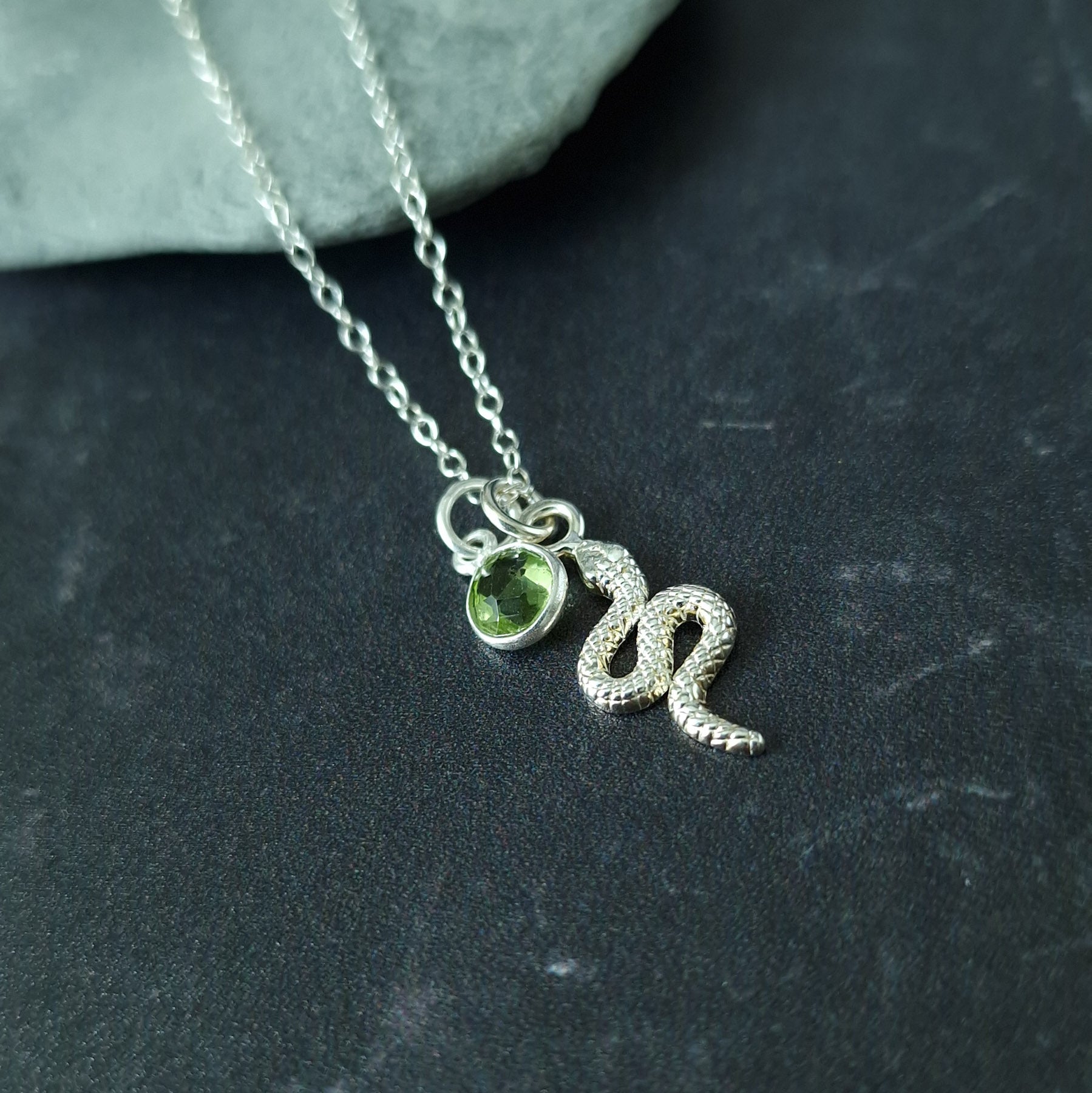 Close up of a silver snake pendant and peridot birthstone necklace