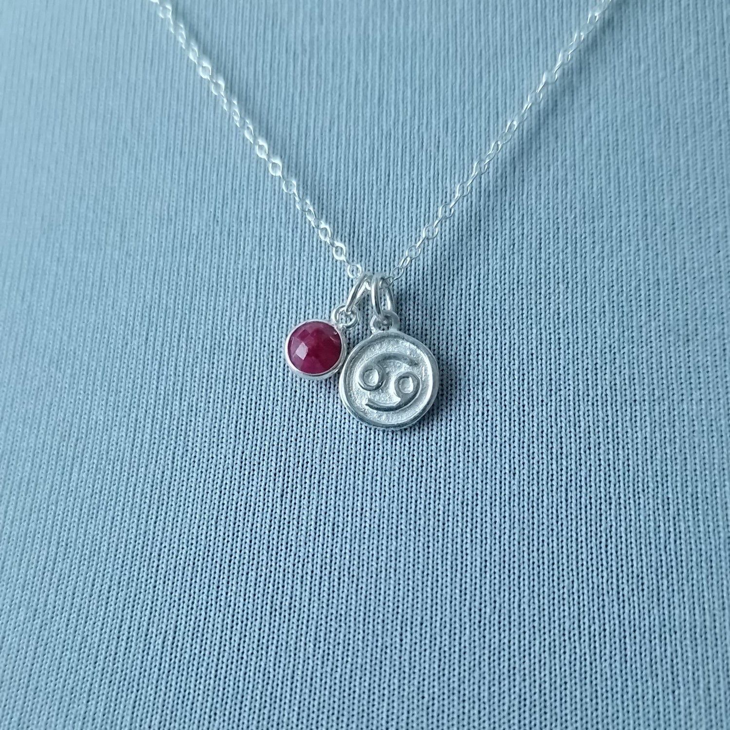 Zodiac Cancer Sign necklace with a ruby birthstone next to it