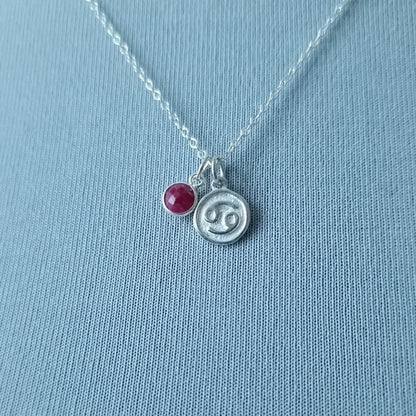 Zodiac Cancer Sign necklace with a ruby birthstone next to it